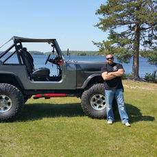 Man standing beside lifted Jeep near lake