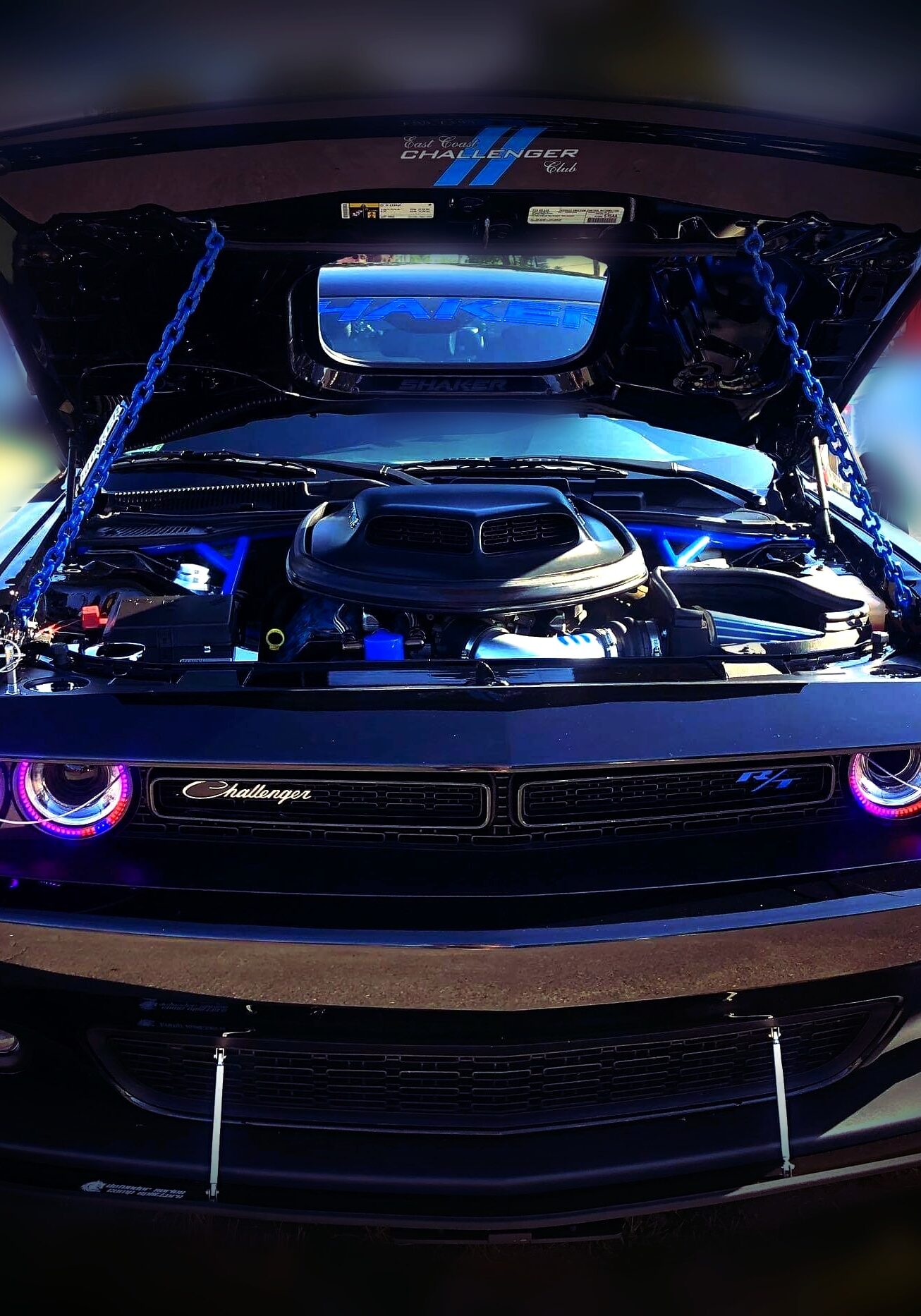 Black Dodge Challenger with open hood, glowing headlights